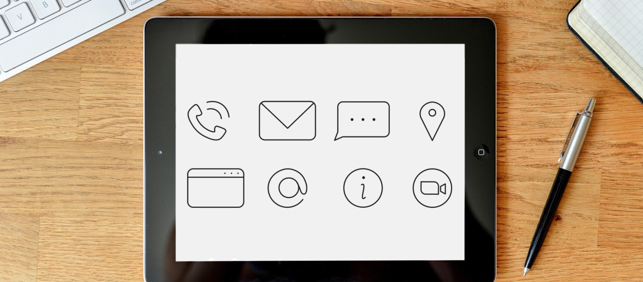 Tablet liegt auf Tisch. Auf diesem typische Kontakt-Symbole wie Telefonhörer, Briefumschlag abgebildet. Rechts von Tablet liegt Stift. Links oben von Tablet ist Tastatur teilweise zu sehen. (Quelle für Konktaktsymbole: Sasiepre / Pixabay.com, https://pixabay.com/de/vectors/symbole-kontakt-kontakt-icons-email-6030813/ )