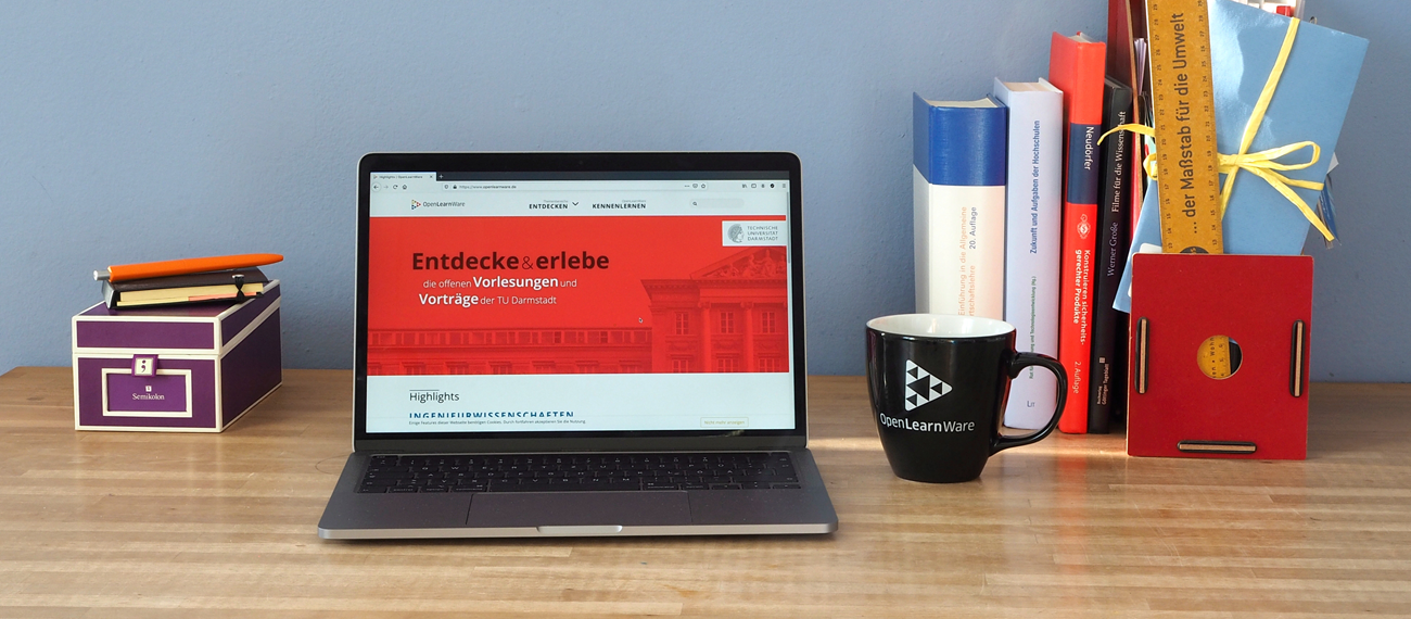 Foto: Ein Schreibtisch mit einem Laptop, auf dem die OpenLearnWare-Seite der TU Darmstadt geöffnet ist. Neben dem Laptop befinden sich eine Tasse mit OpenLearnWare-Logo, Bücher, ein Ordner und ein Stift.