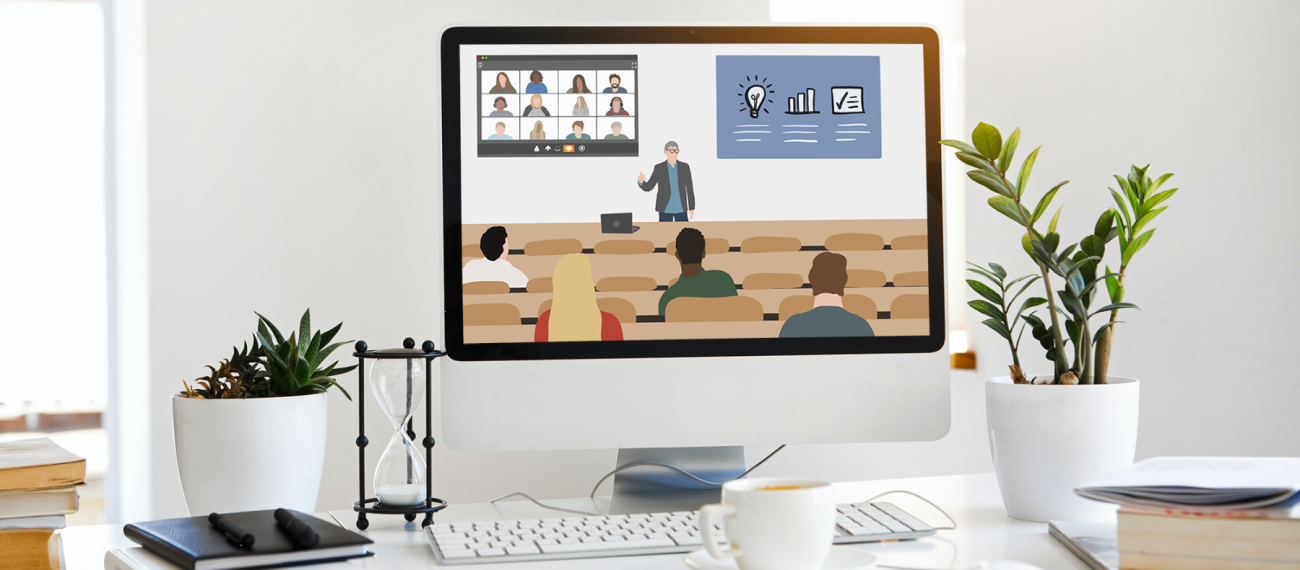 Foto: Schreibtisch mit Monitor, auf dem Hörsaal zu sehen ist, wo Lehrperson eine Präsentation zeigt und weitere Studierende online zugeschaltet sind.