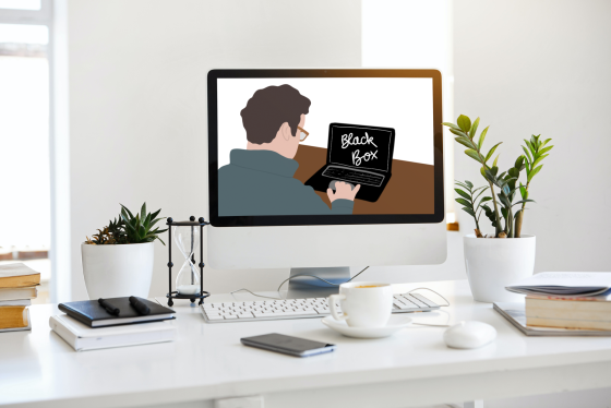 Foto: Schreibtisch mit Monitor, auf dem eine Person zu sehen ist, die auf eine Black Box schaut